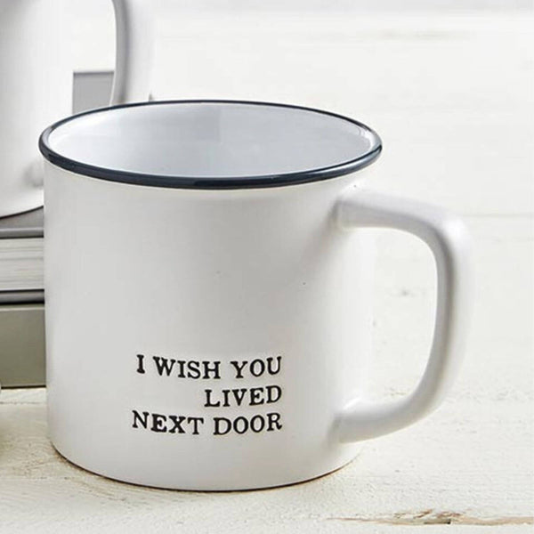 White mug with black text 'I WISH YOU LIVED NEXT DOOR' on a light wooden surface.