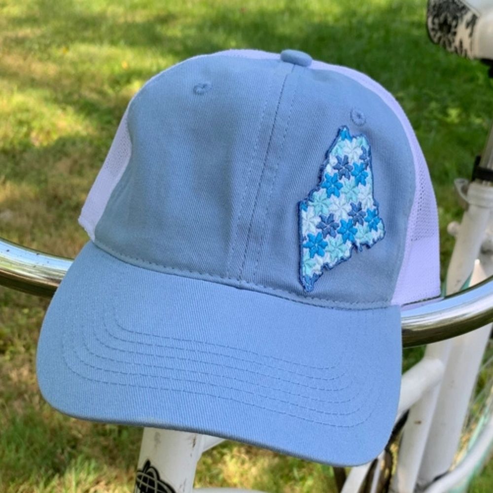 Blue and beige cap with floral Maine state design on a white background