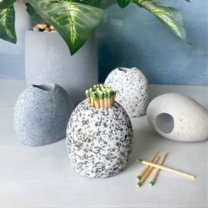 A collection of four natural stones in different gray and white tones used as match strikers, styled near a potted plant.