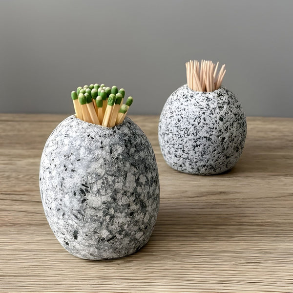 Two natural stone holders on a wooden surface; one in the foreground holds matches, and one in the background holds toothpicks.