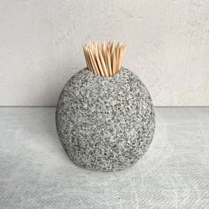 A single, round, gray speckled stone holder standing on a white surface, filled with a bundle of wooden toothpicks.