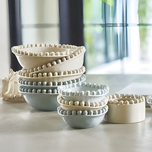 Stacked ceramic beaded bowls in blue and neutral tones styled on kitchen counter near window.