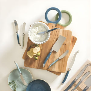 Blue-handled stainless steel cheese spreaders styled on a charcuterie board with dips and crackers