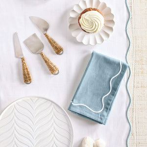 Blue embroidered scalloped cotton napkin folded on table, paired with a white scalloped table runner.