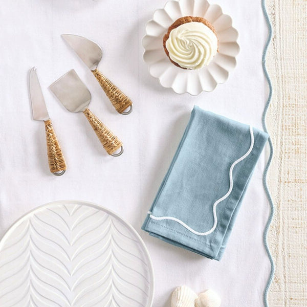 Blue embroidered scalloped cotton napkin folded on table, paired with a white scalloped table runner.