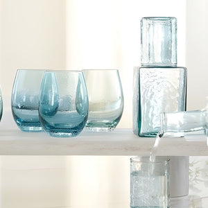 Blue seeded stemless wine glasses with subtle air bubbles styled on shelf with matching glass carafe.