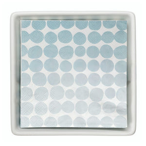 Stack of blue dot paper cocktail napkins inside white ceramic tray.