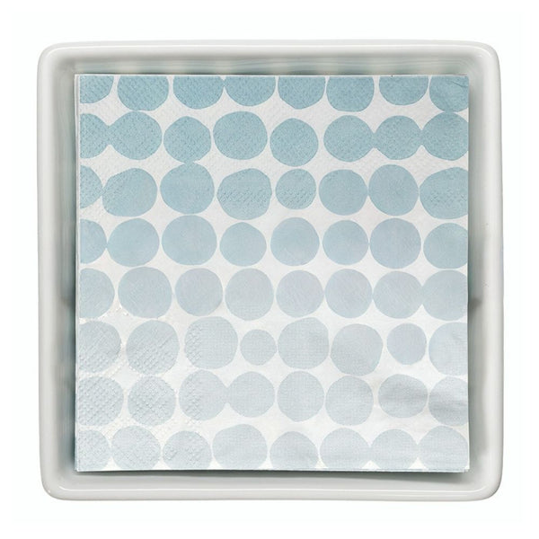 Stack of blue dot paper cocktail napkins inside white ceramic tray.