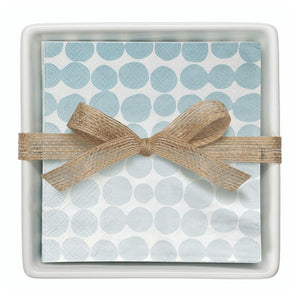 Stack of blue dot paper cocktail napkins tied with burlap ribbon inside white ceramic tray.