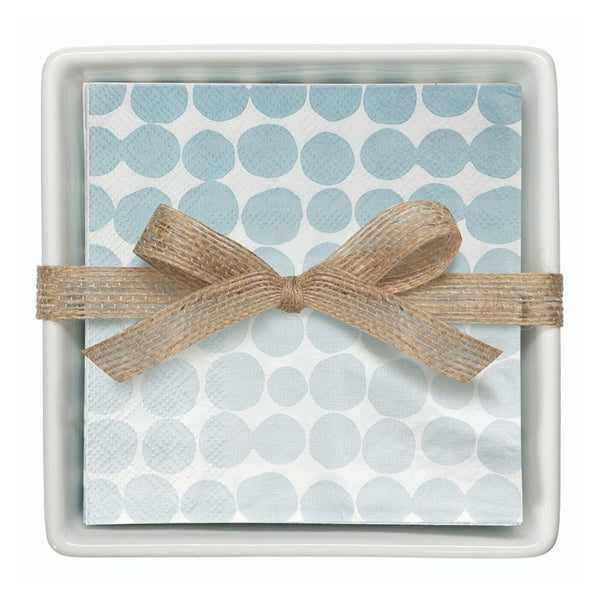Stack of blue dot paper cocktail napkins tied with burlap ribbon inside white ceramic tray.