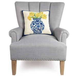 Square hand-hooked wool pillow featuring a blue-and-white patterned ginger jar filled with bright yellow daffodils, set on a light gray chair