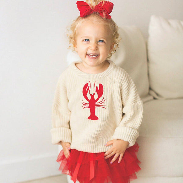 Toddler wearing chunky knit lobster sweater with red tutu skirt and red ribbon
