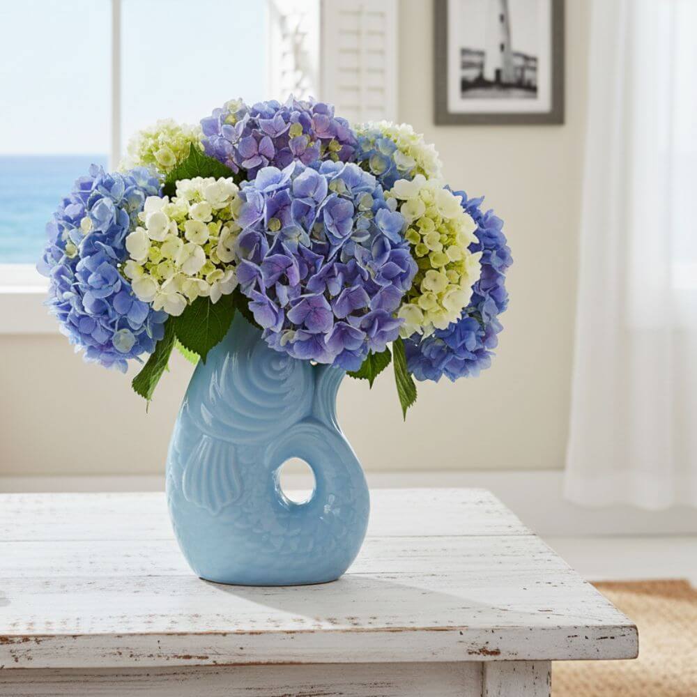 Blue ceramic vase with a circular hole on a white surface, containing a bouquet of blue and green hydrangeas.