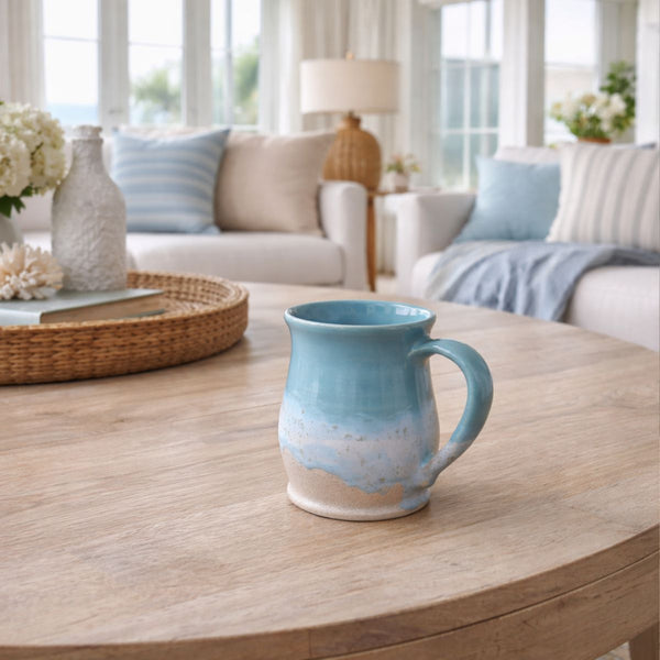 Handcrafted coastal mug with layered blue glaze over natural stoneware, smooth curved rim, perfect for coffee or tea.