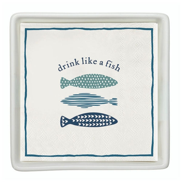 Cocktail napkins with “Drink Like a Fish” fish design placed in a white ceramic napkin tray
