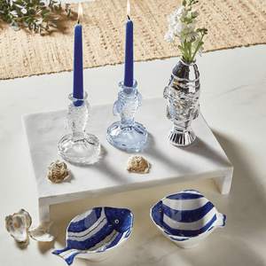 Decorative fish-themed setting with blue candles, a silver fish vase, and blue-and-white ceramic fish bowls on marble.