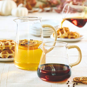 Glass pitchers with natural rattan handle placed on table, with drinks to serve