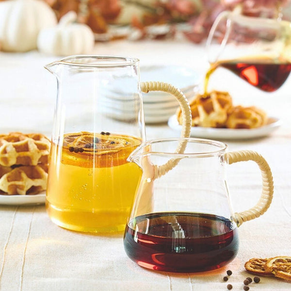 Glass pitchers with natural rattan handle placed on table, with drinks to serve
