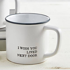 White mug with black text 'I WISH YOU LIVED NEXT DOOR' on a light wooden surface.