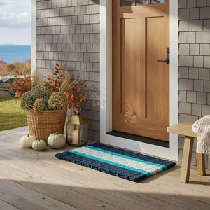 Front door with a Navy, Teal, Seafoam Striped doormat on a wooden deck, featuring decorative elements.