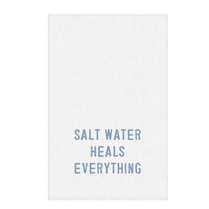 Flat lay of white cotton towel with coastal blue “Salt Water Heals Everything” lettering
