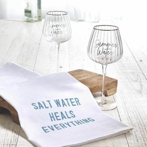 White cotton “Salt Water Heals Everything” towel styled on table with summer wine glasses