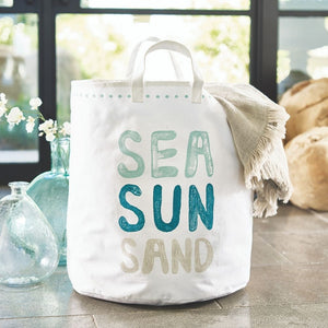 Large cotton canvas tote bag with Sea Sun Sand lettering styled with coastal decor and glass vases