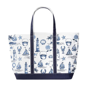Front view of a white canvas tote bag with a dark navy blue base and handles, featuring a blue repeating pattern of coastal motifs like sailboats, lighthouses, and lobsters.