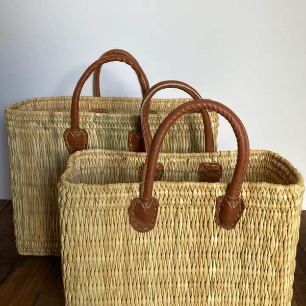 Two woven baskets with brown handles on a wooden surface.