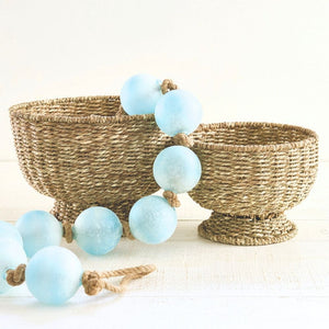 Small round handwoven seagrass basket with natural texture, 9 inches diameter, paired with a large round seagrass basket and light blue garlands.