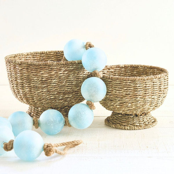 Small round handwoven seagrass basket with natural texture, 9 inches diameter, paired with a large round seagrass basket and light blue garlands.
