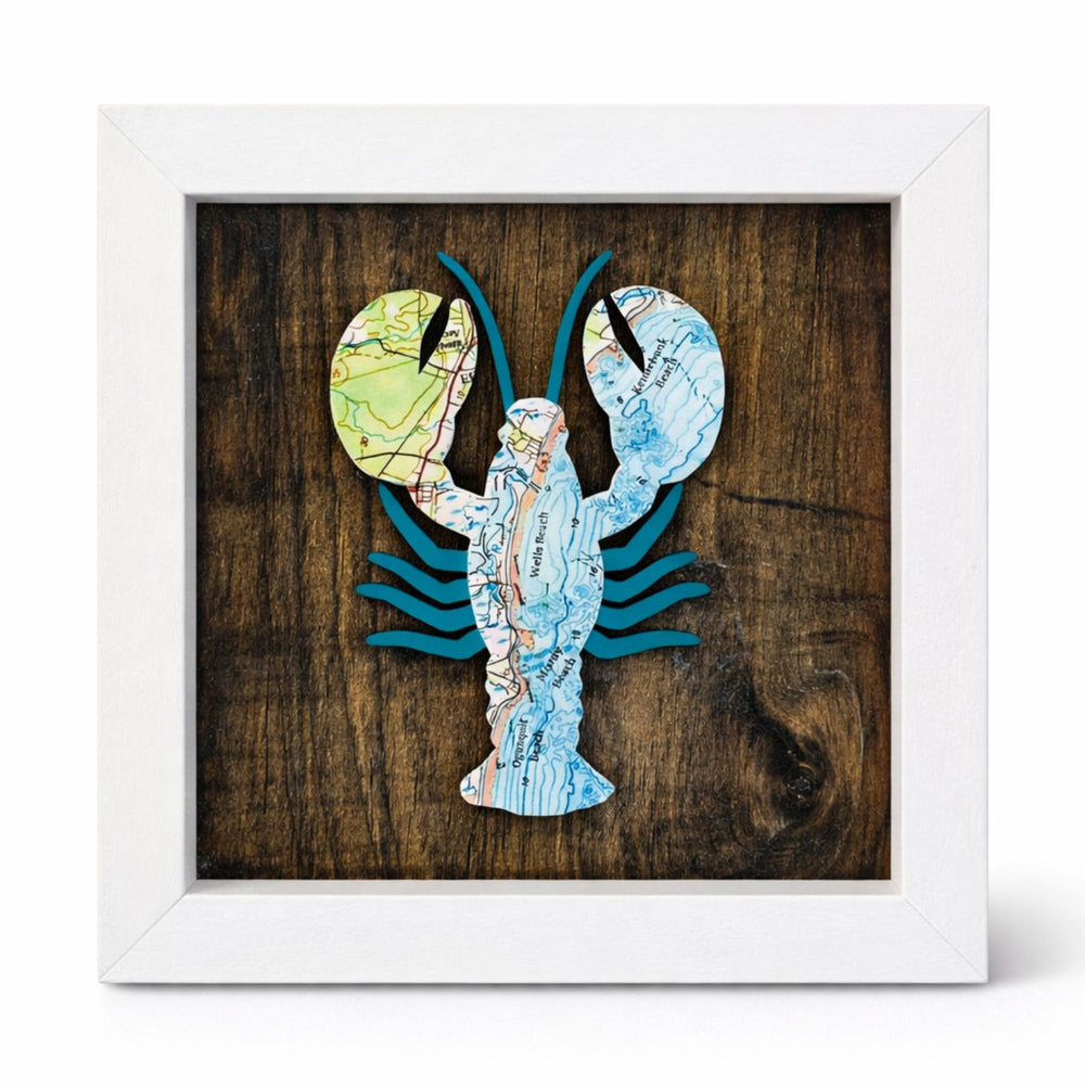 Framed artwork of a lobster made from nautical chart map pieces on a wooden background with a white wood frame