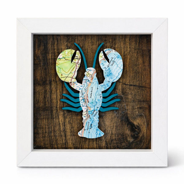 Framed artwork of a lobster made from nautical chart map pieces on a wooden background with a white wood frame