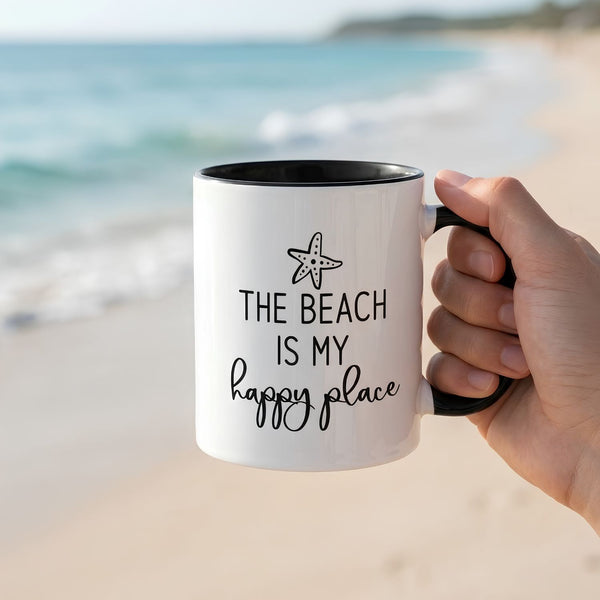 White Ceramic Coffee Mug With Black Interior and Handle Featuring The Beach Is My Happy Place Quote, Held Against a Sandy Beach and Ocean Background, Coastal Mugs, Beach House Gifts